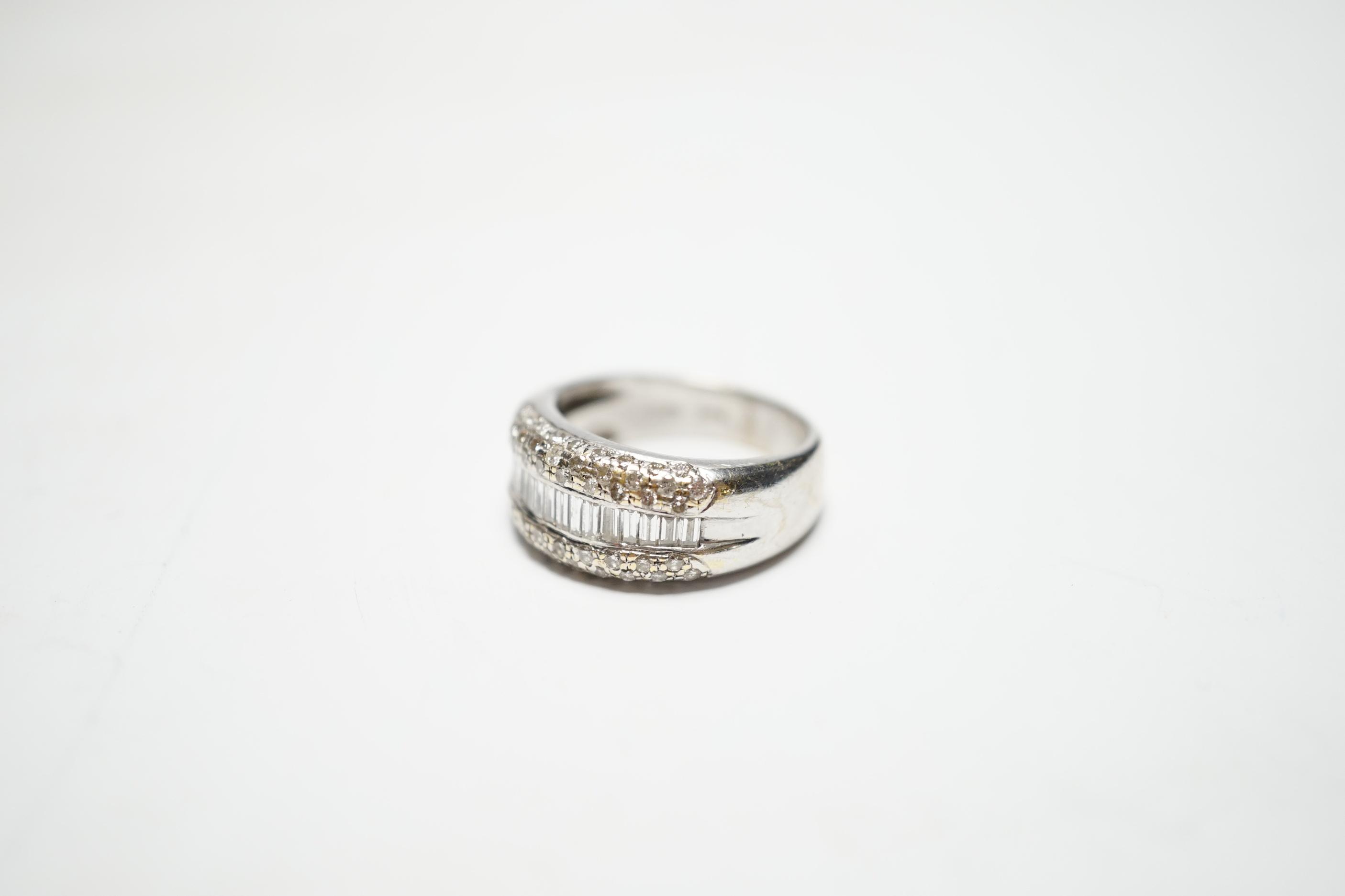 A modern 750 white metal and graduated baguette cut diamond set half hoop ring, with diamond chip set borders, size N, gross weight 9.3 grams.